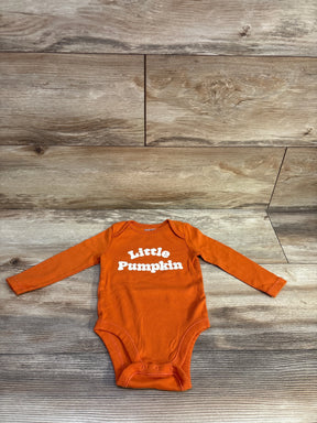 Front view of an orange Old Navy Little Pumpkin long sleeve bodysuit with white Little Pumpkin lettering on a wood floor