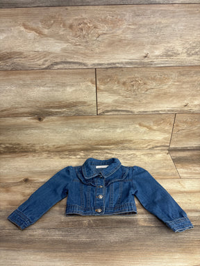 Children's blue denim jacket with buttons and ruffle detail laid on wooden floor background