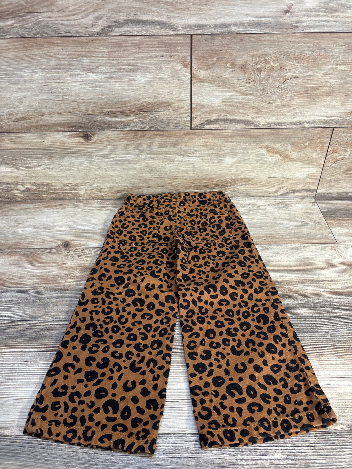 Flat lay of girls' Cat and Jack brown leopard-print wide-leg jeans showing wide legs and elastic waistband on light wood floor background