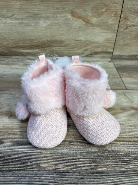 Front view of pink knit baby booties with faux fur cuffs and pom-pom accents on wood background