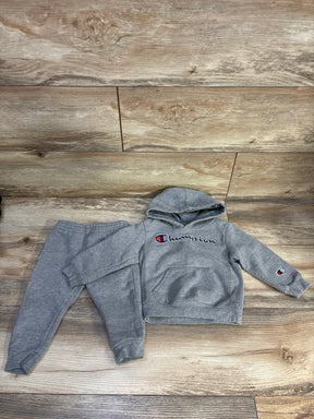 Grey Champion hoodie and joggers set laid flat, front view showing logos on chest and sleeve, front pocket on wood floor
