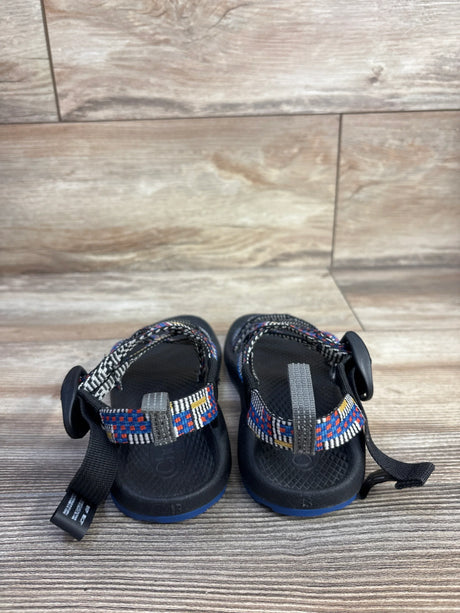 Rear view of Chaco ZX/1 Ecotread toddler sandals in black showing multicolor woven straps and blue-trim soles on wood floor