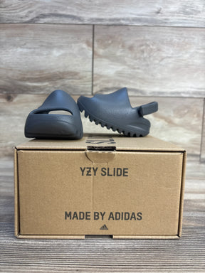 Gray Adidas YZY Slide sandals for kids displayed on cardboard shoe box, wood background
