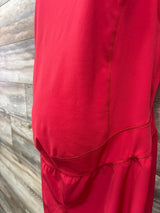 Close-up side view of Isabel maternity active romper showing red fabric, ruched belly panel and seams on wood background