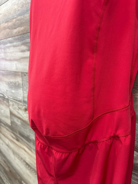 Close-up side view of Isabel maternity active romper showing red fabric, ruched belly panel and seams on wood background