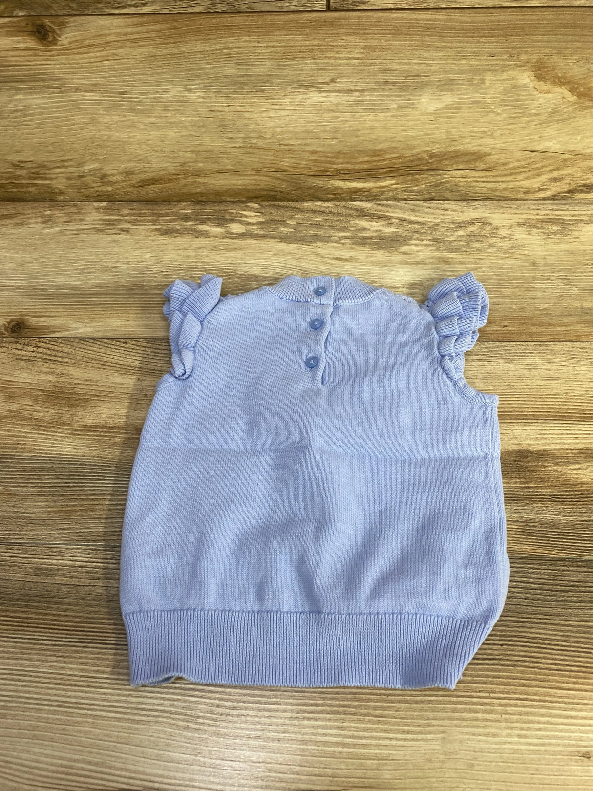 Flat-lay of blue Janie & Jack Skyline crochet sleeveless top size 3T showcasing ruffle sleeves, back button placket and ribbed hem on wood background