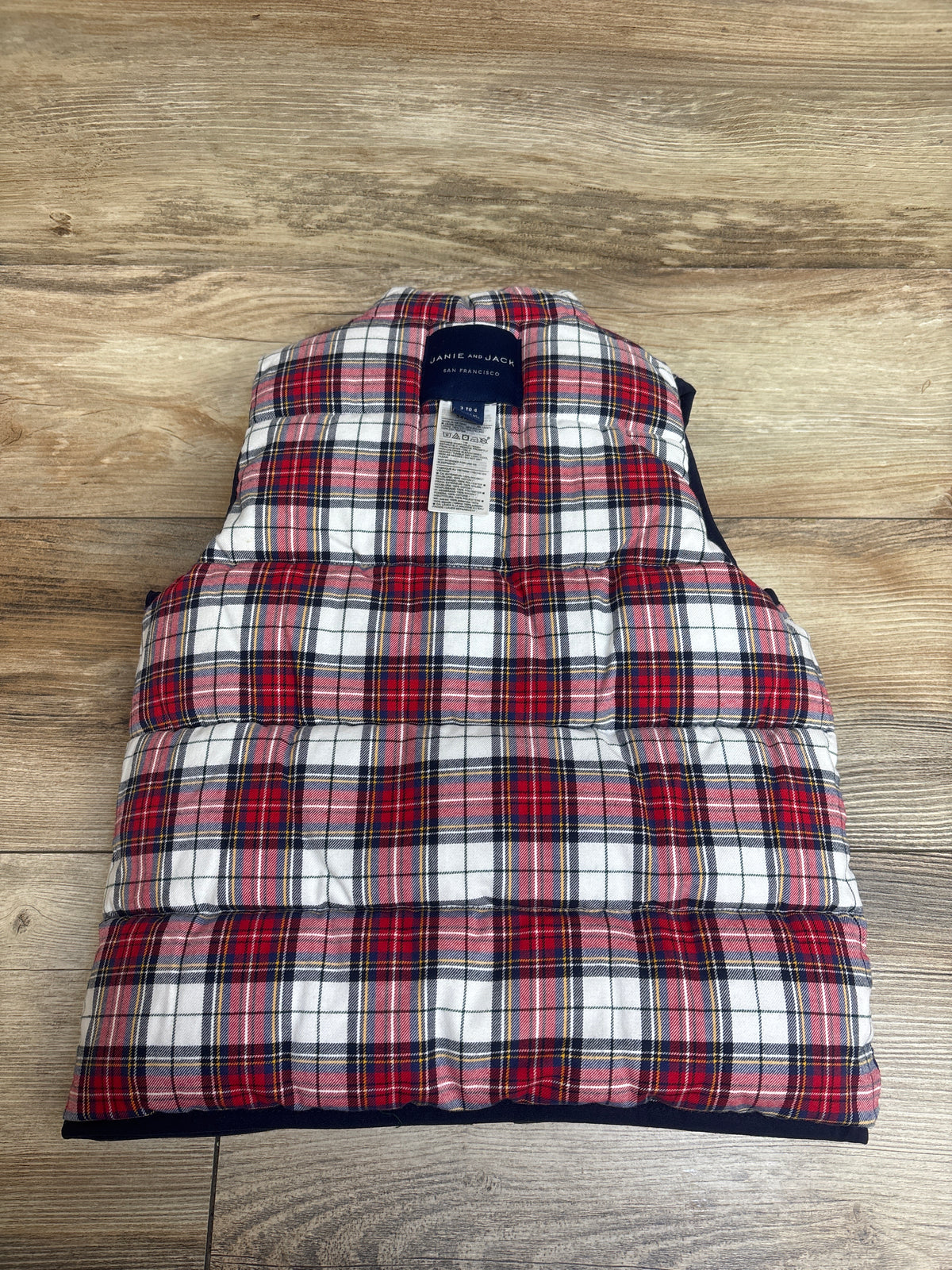 Back view of Janie & Jack reversible red tartan puffer vest on a wood surface