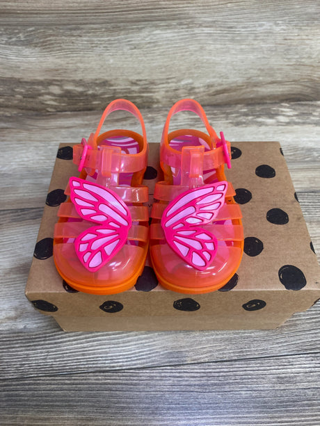 Top-down view of Sophia Webster toddler jelly sandals showcasing pink butterfly appliqués and translucent orange straps on a brown polka-dot box