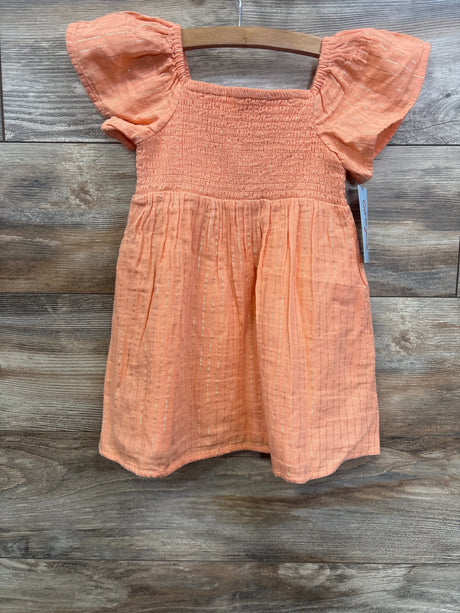 Peach toddler dress with flutter sleeves and gold thread accents on wood background
