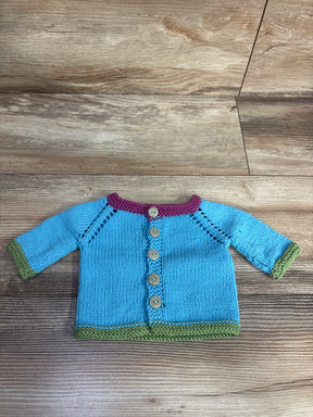 Handmade baby cardigan in blue knit with green cuffs and hem, purple neckline, and wooden buttons on wood surface