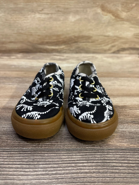 Front view of Vans Authentic dinosaur skeleton sneakers showcasing black uppers, white skeleton print, black laces, and gum soles on a wood floor