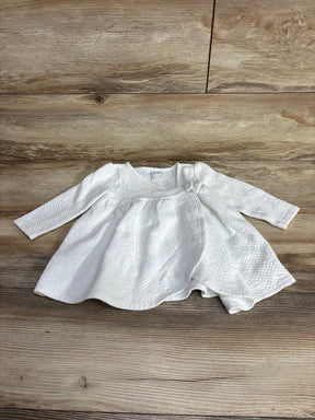 White textured long sleeve baby dress with bow detail, laid flat on wood background