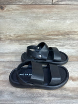 Three-quarter view of MGBABY black foam sandals size 11/12c showing two wide straps and snap heel strap on wood background