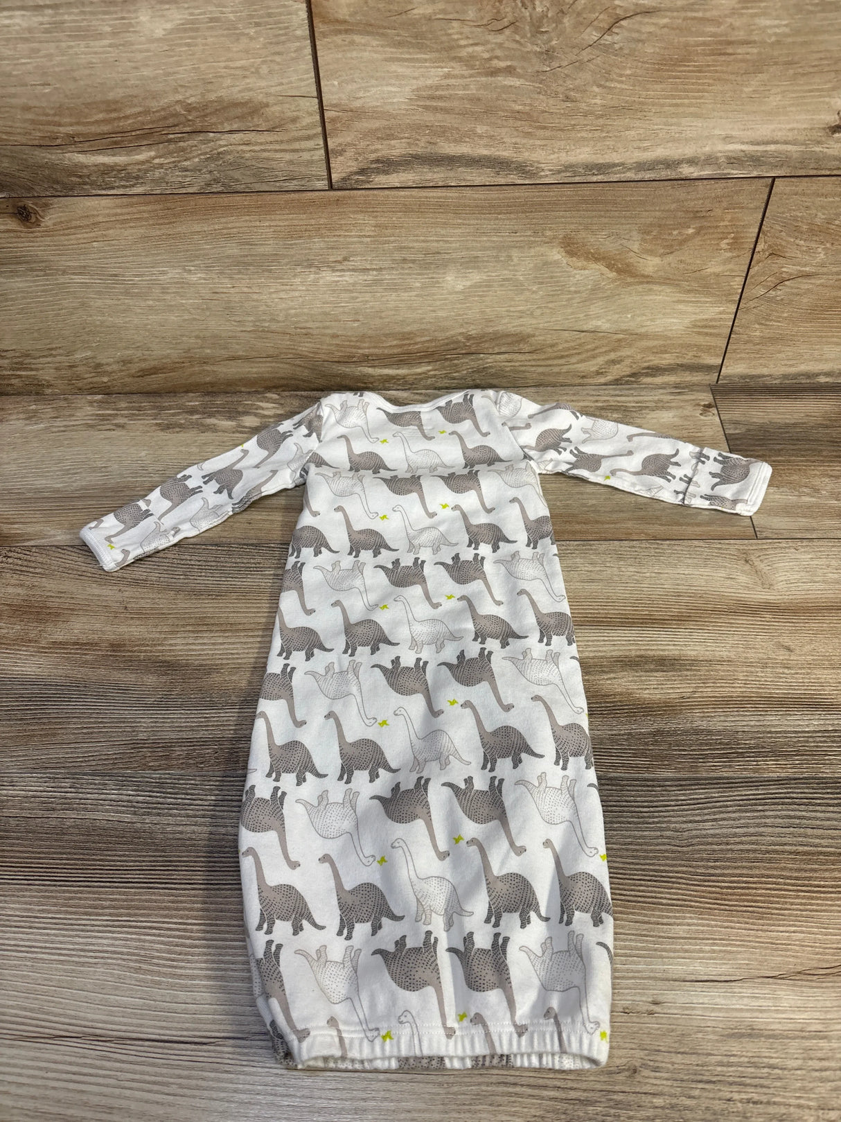 Flat lay of newborn white Simple Joys gown with gray dinosaur print, long sleeves and elastic bottom on wood floor