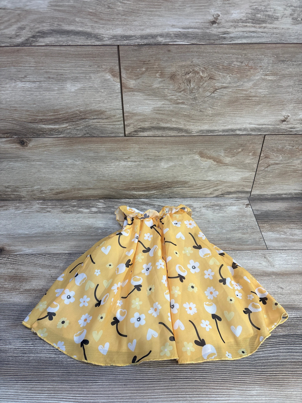 Flat lay of Baby Starters yellow tulle bodysuit dress showcasing gathered waist and floral and heart print skirt on wood background
