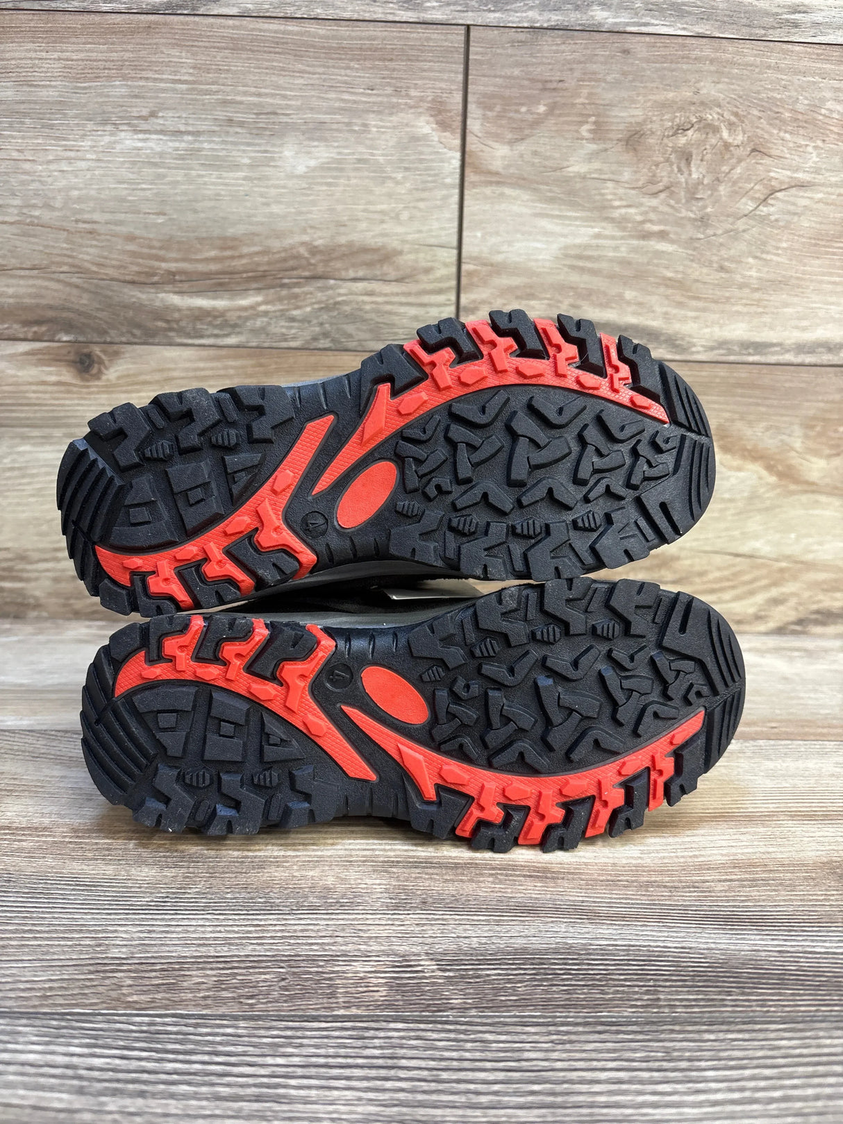 Kids black and red hiking shoe soles with rugged tread on wood background