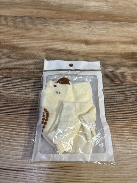 Top-down view of cream baby knee pads showcasing brown non-slip grip dots in clear plastic packaging on wood surface