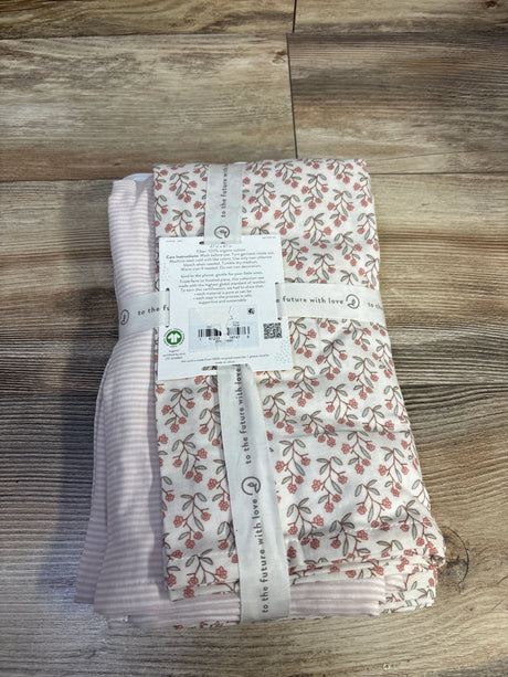 Top view of two Little Planet muslin swaddle blankets folded, pink floral and pink stripe, tied with ribbon on wood table