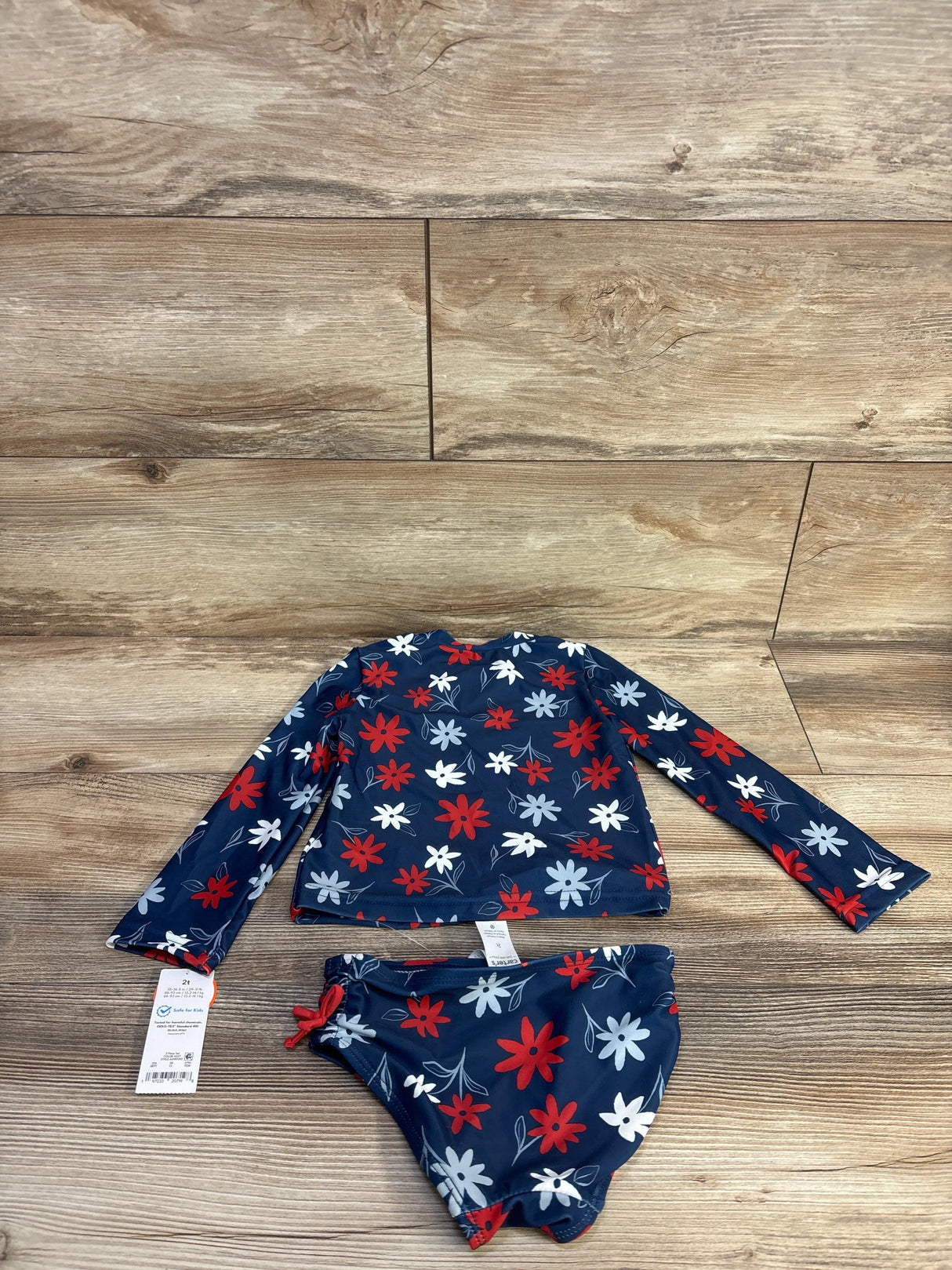 Top-down view of navy girls' two-piece rash guard and bikini bottoms with red and white floral print on wood floor