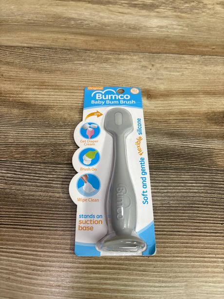 Front view of Bumco Baby Bum Brush in grey packaging showcasing flexible silicone and suction base on a wood surface
