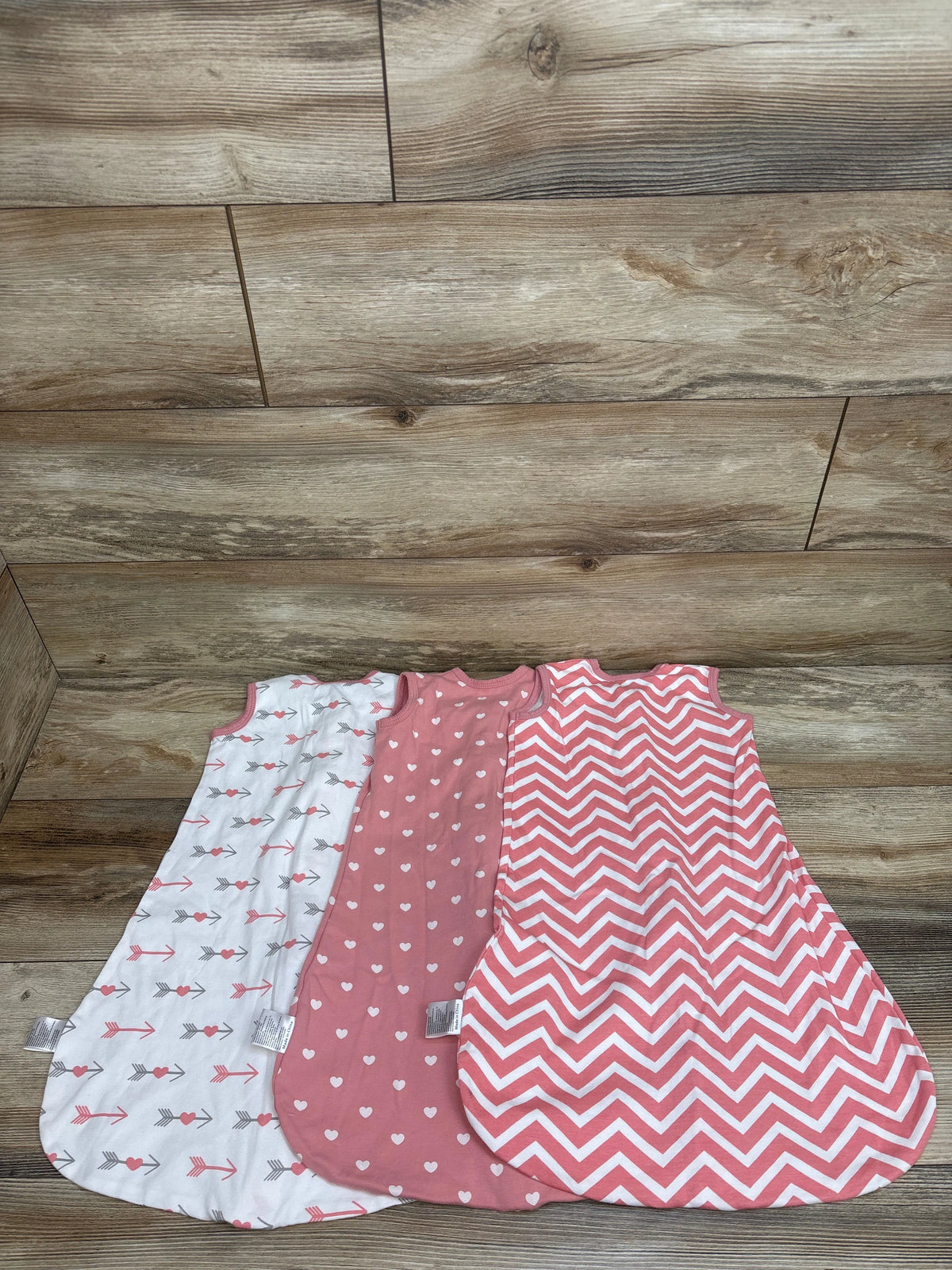 Top view of three Yoofoss sleep sacks in white and pink, showcasing arrow, heart, and chevron patterns on a wood background