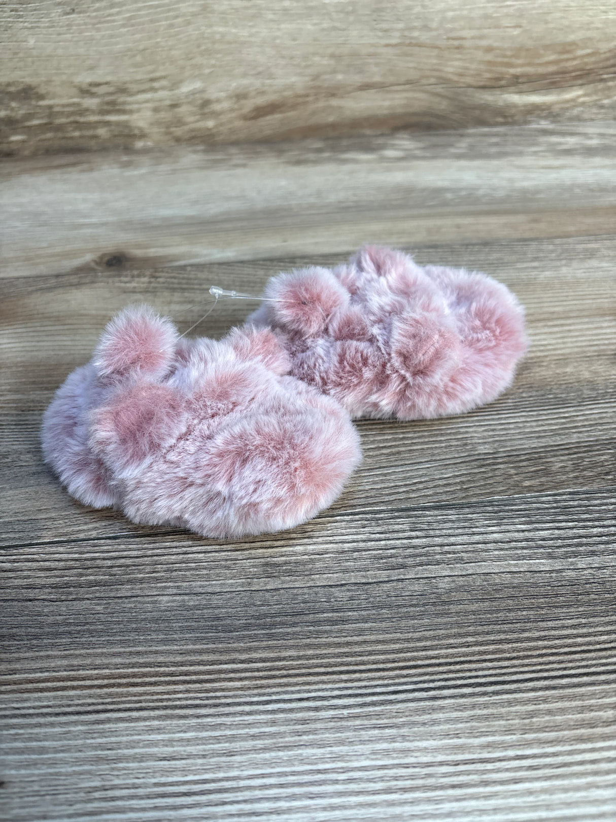 Pink fuzzy baby booties on wooden background, soft infant footwear