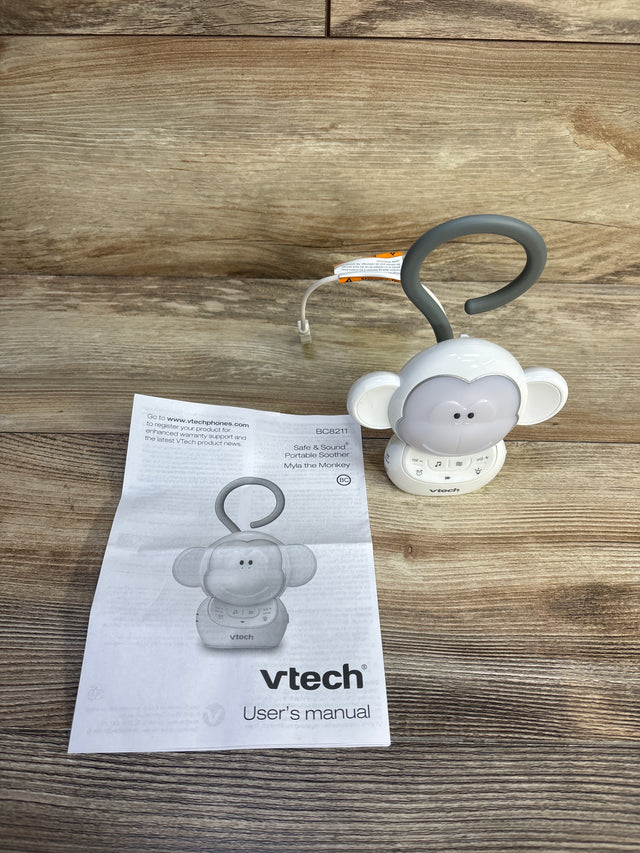 Front view of VTech Myla the Monkey soother, white, showing hanging loop and control buttons on wooden tabletop