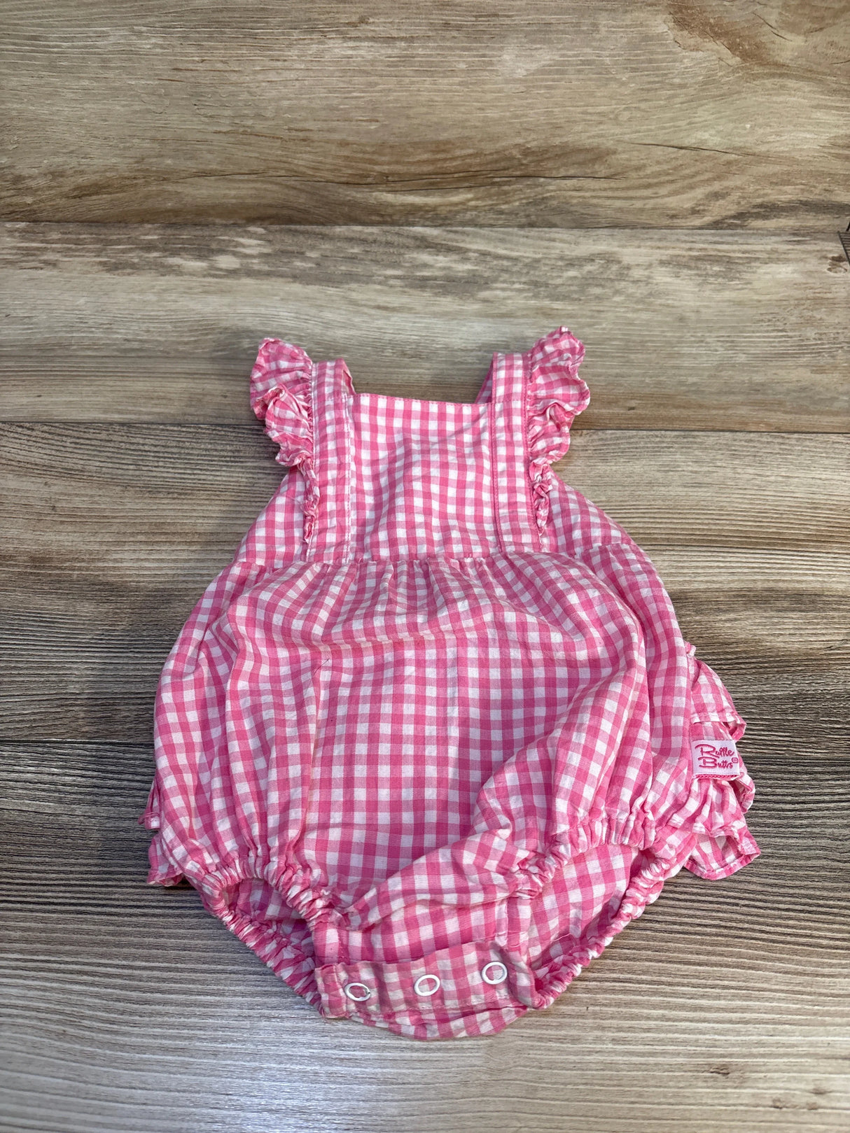 Pink gingham baby romper with ruffles, perfect for newborns and infants, laid on wood floor