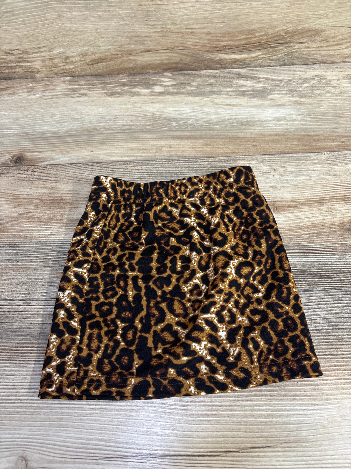Flat lay of toddler leopard-print skirt showing elastic waistband and brown-black pattern on wooden floor