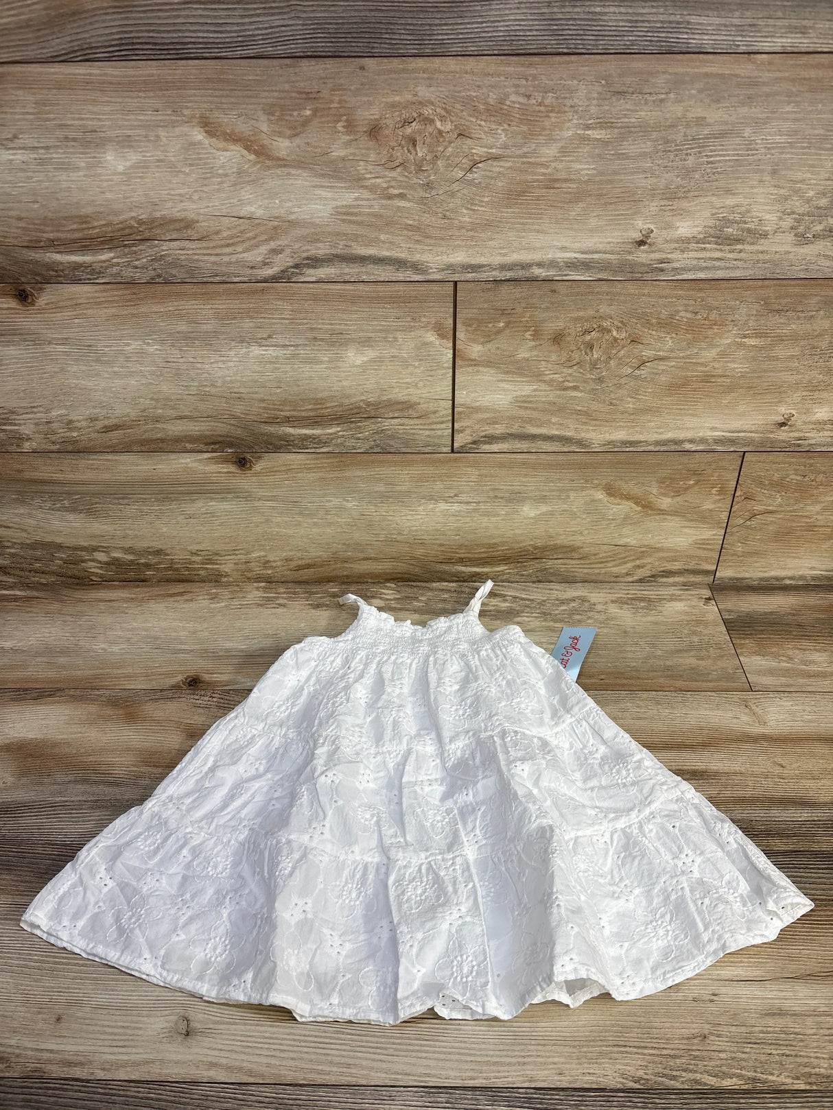 Top-down of white eyelet embroidered dress (Cat & Jack 2T) showing smocked bodice, thin straps and tiered skirt on wood floor