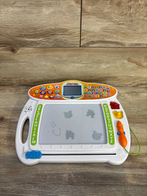 Front view of VTech Write & Learn showing magnetic drawing board, orange tethered stylus, and control panel screen