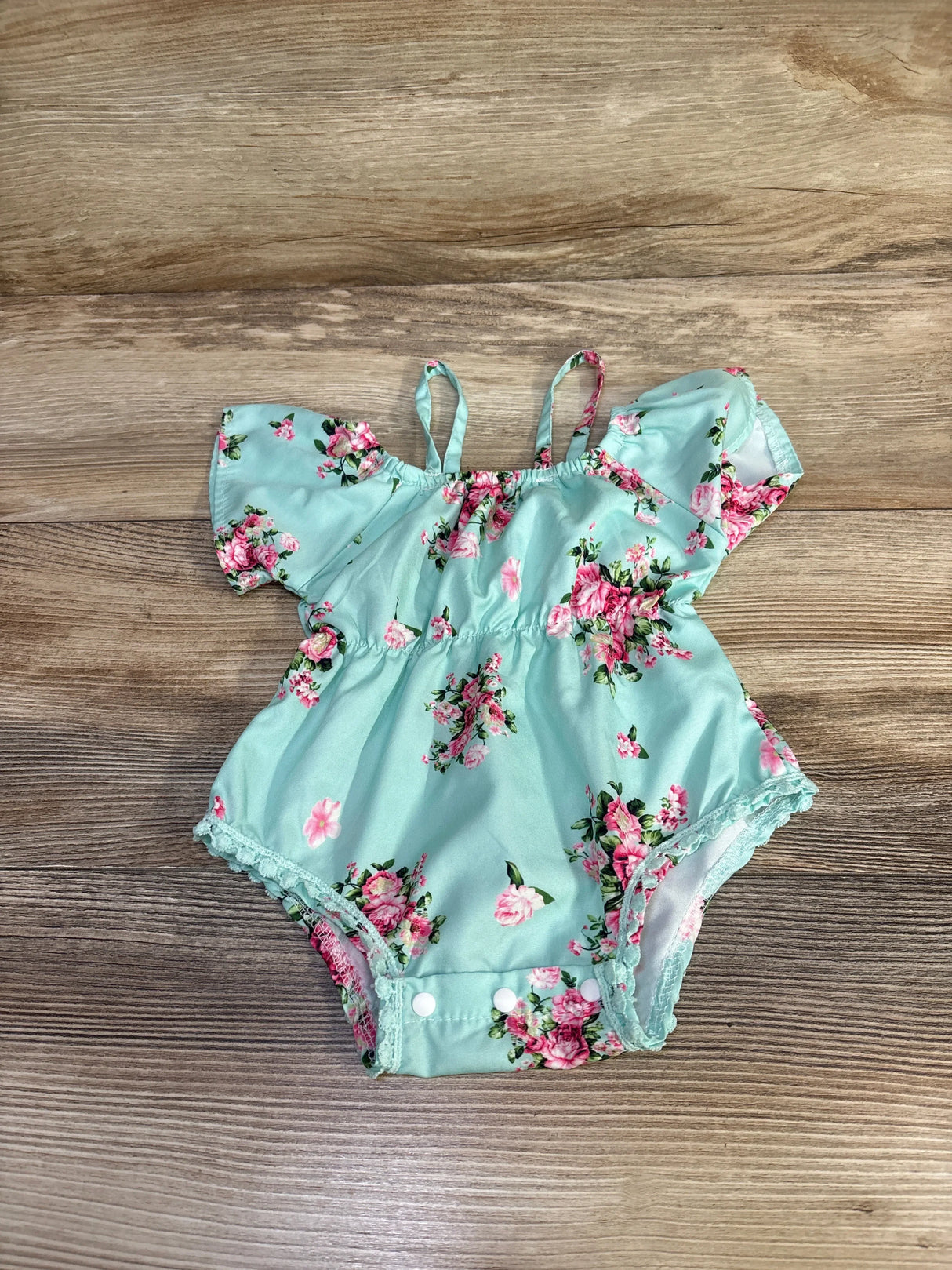 Top-down view of mint blue floral off-shoulder baby romper with ruffled sleeves and snap crotch on wood background