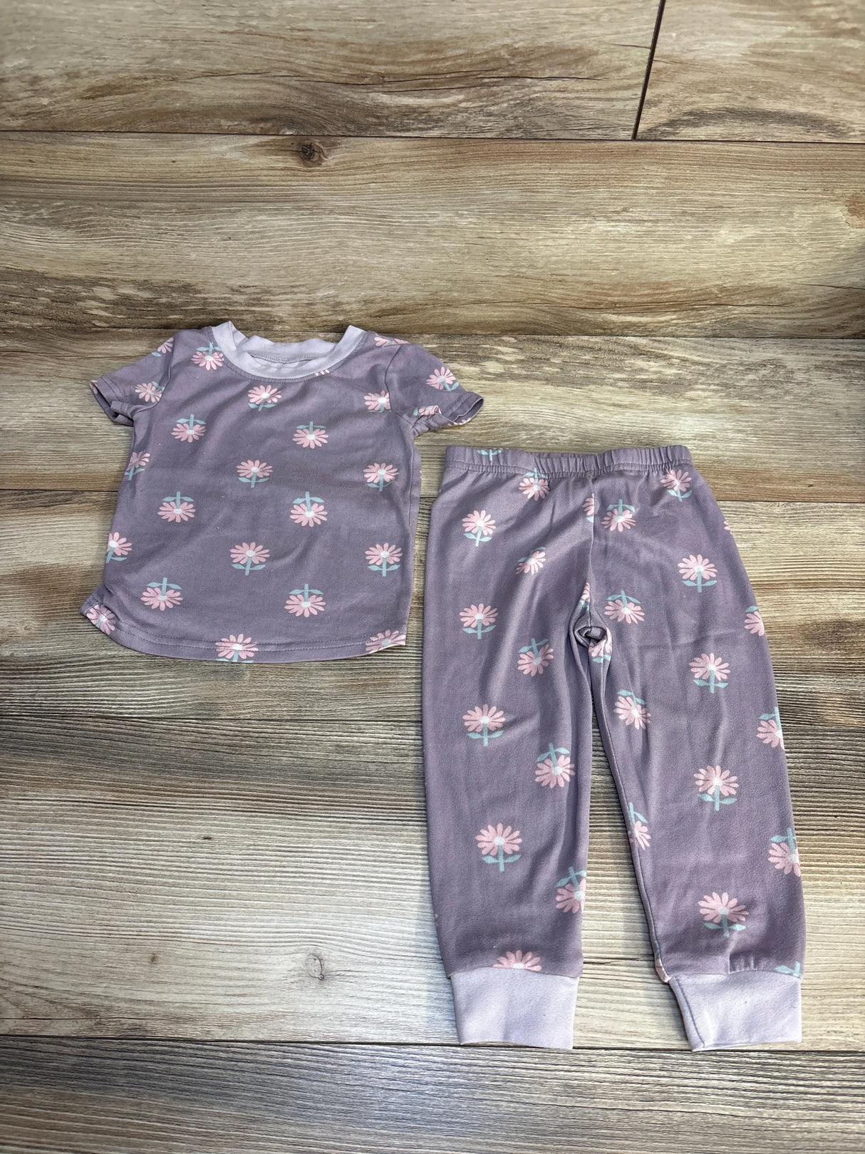 Purple floral toddler pajama set with short sleeves and elastic waist pants on wood floor