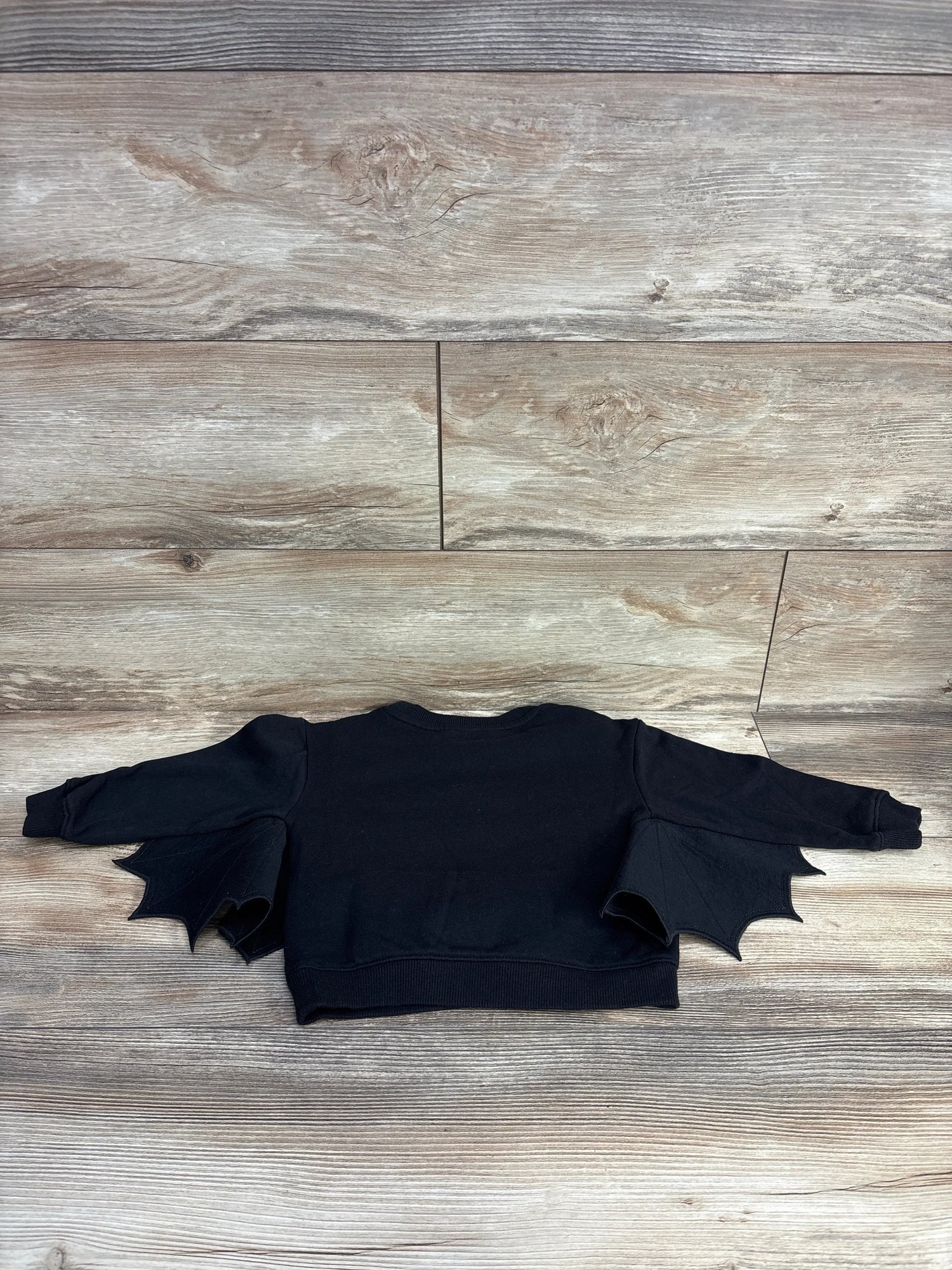 Black bat-wing kids sweater on wooden floor, perfect for Halloween or playful outfits.