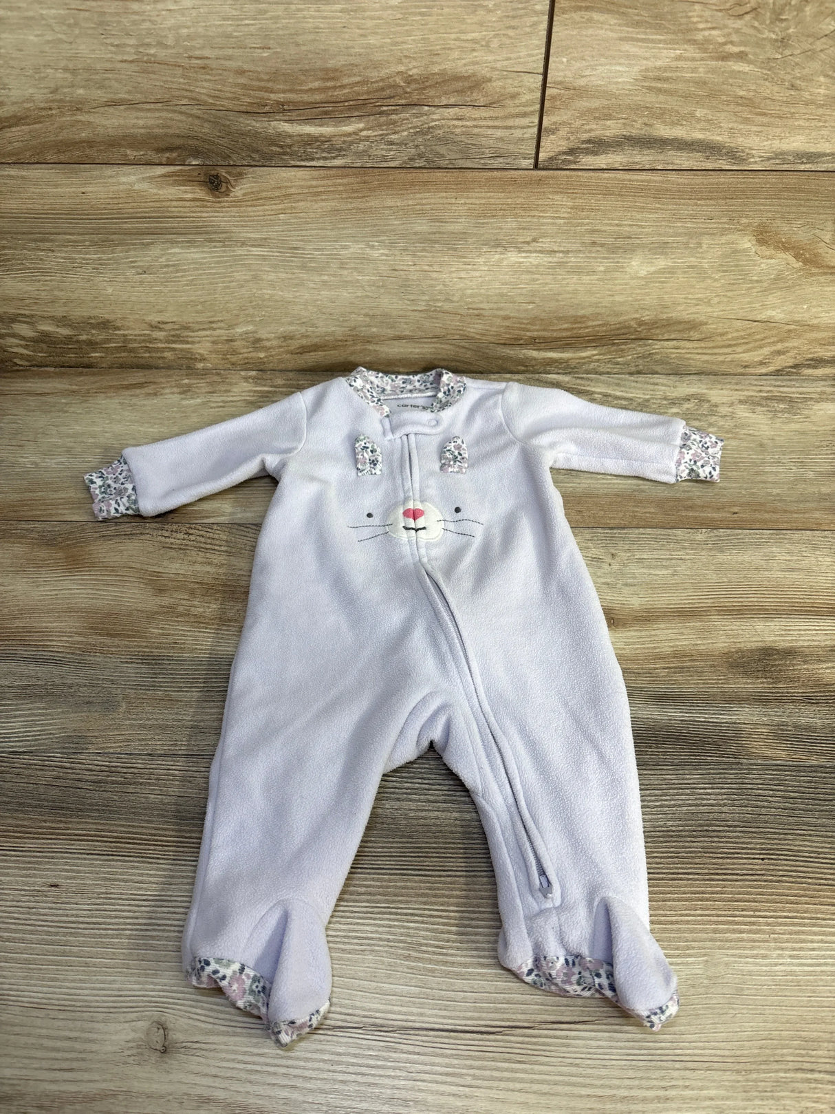 Flat lay of lilac Carter's blanket sleeper, 3 months, showing embroidered bunny face, diagonal zipper and floral-trimmed cuffs on wood floor