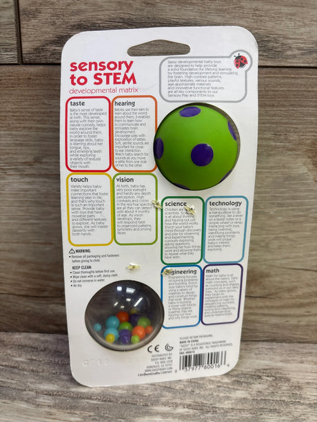 Back view of Sassy Spin Shine Rattle package showing a green and purple ball with colorful beads on a wooden surface