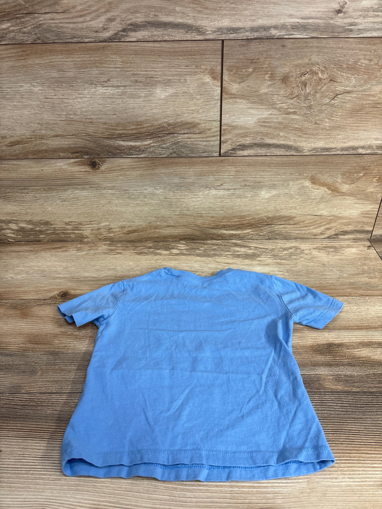Light blue short-sleeve kids t-shirt laid flat on wooden surface at children's resale store