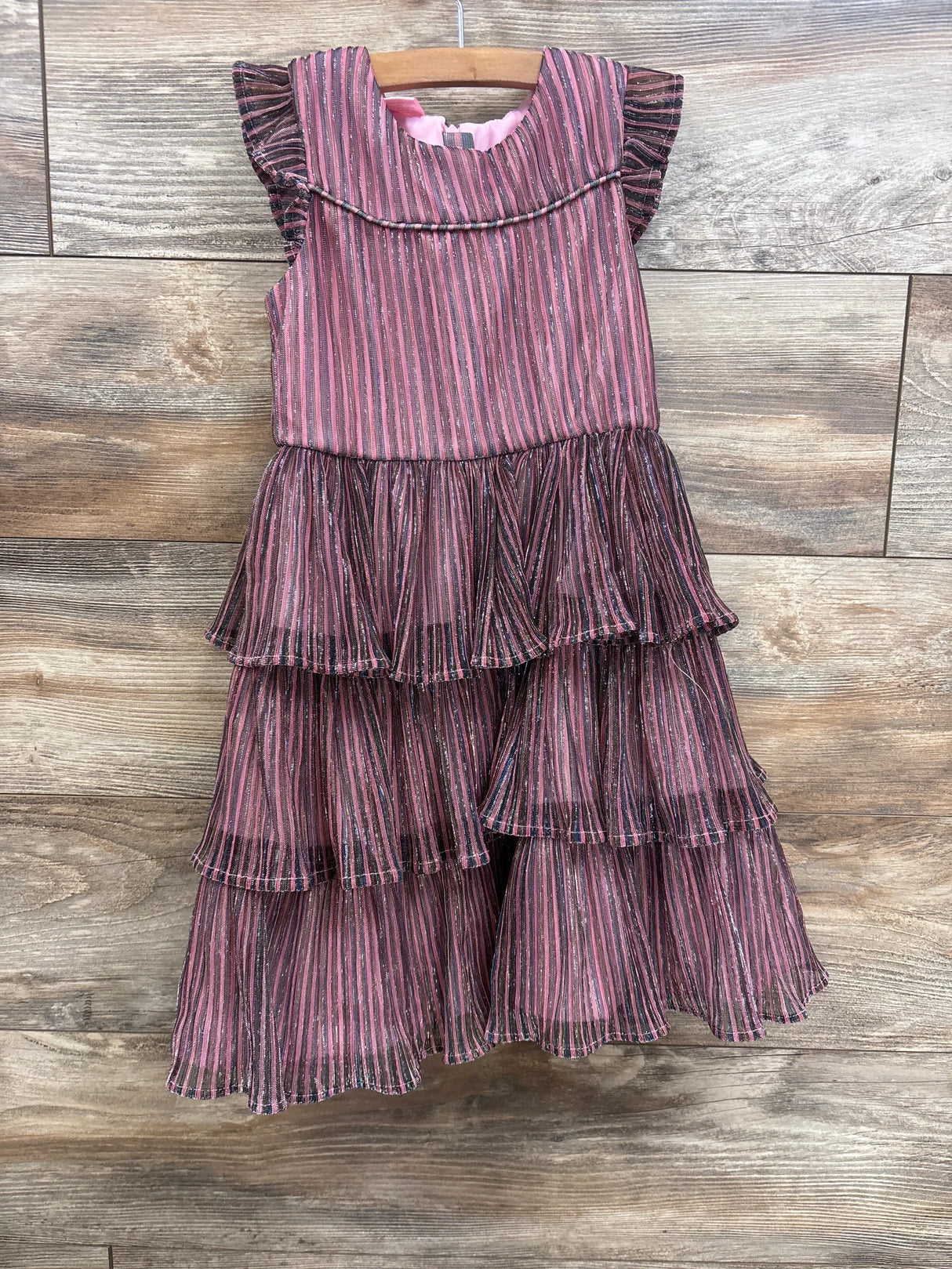 Pink and black striped tiered ruffle dress for girls, hanging on wooden hanger against wood floor
