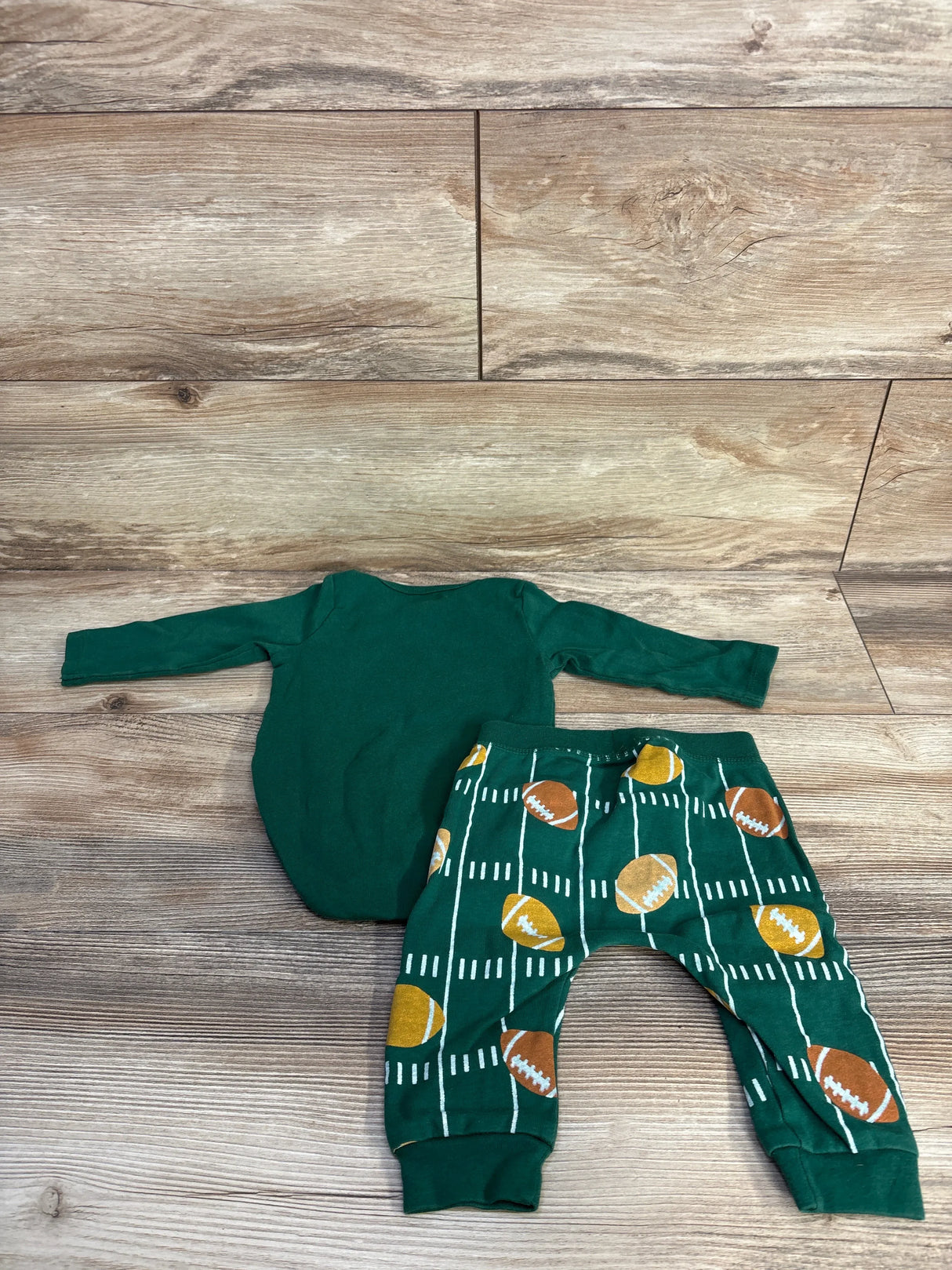 Flat lay of green 2-piece baby bodysuit and pants set with long sleeves and football-print pants on wood background