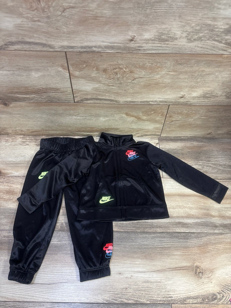Top-down view of Nike two-piece satin tracksuit showcasing black zip-front jacket and matching pants with a wood-grain floor background