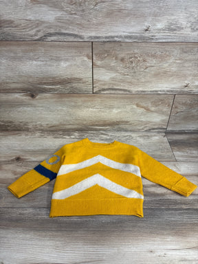 Yellow kids sweater with white chevron stripes and blue circle, laid on wooden floor