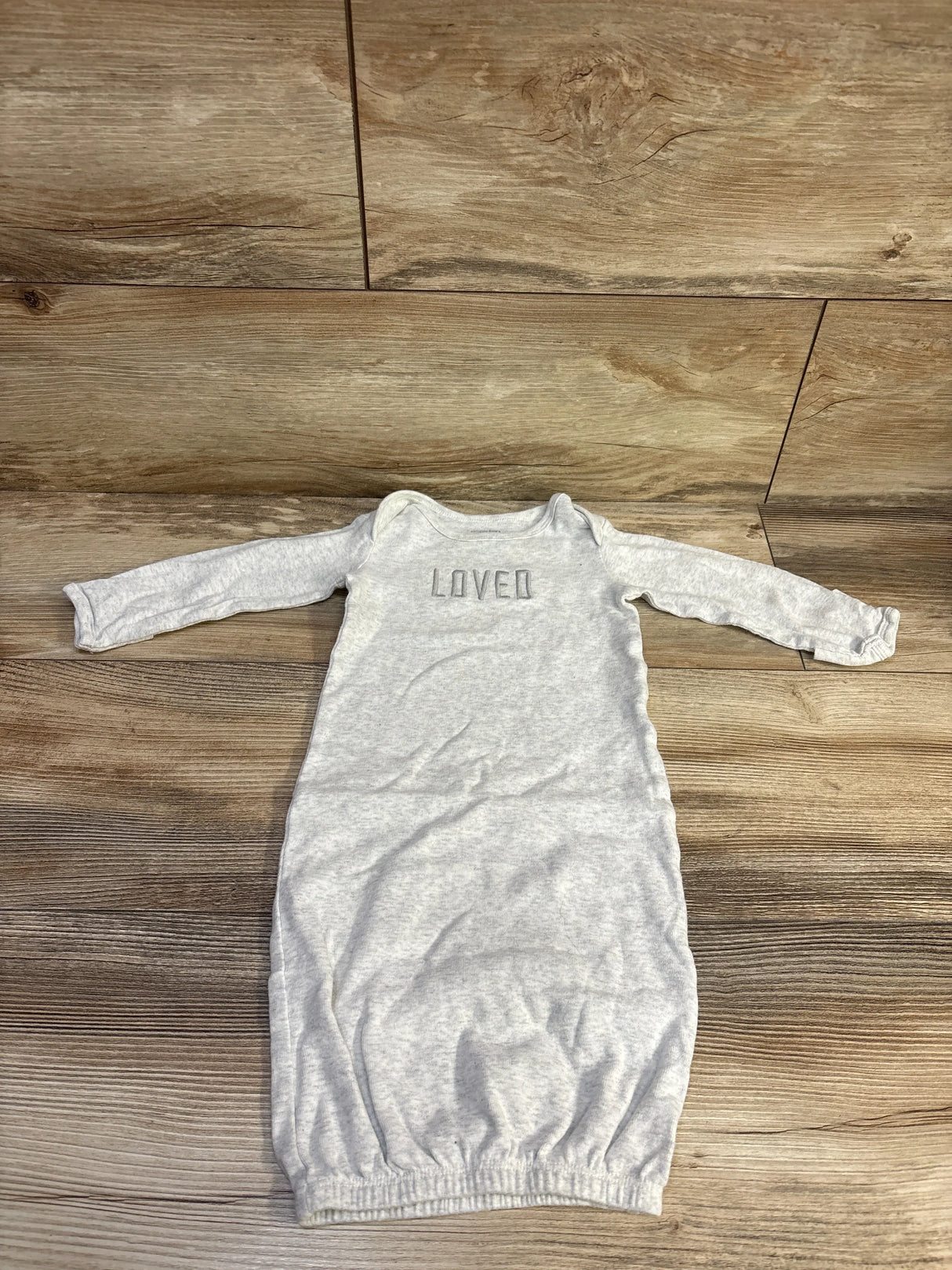 Flat lay of grey Simple Joys newborn gown showing long sleeves, LOVED chest embroidery, and elasticized bottom on wood floor