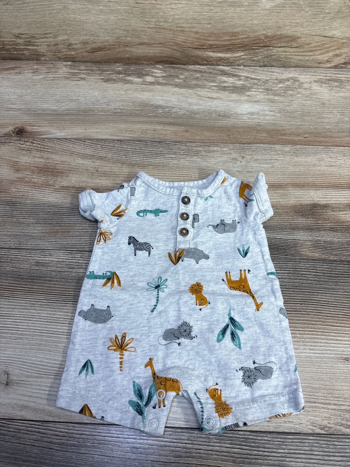 Flat lay of newborn grey Henley shortie romper with three wooden buttons, animal print, and snap crotch on wood background