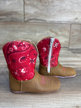 Infant brown cowboy boots with red paisley fabric and zipper on wood background.