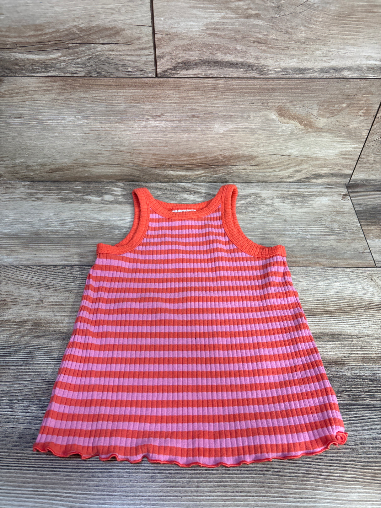 Flat lay of girls ribbed tank top showing pink and orange horizontal stripes and lettuce-edge hem on wood background