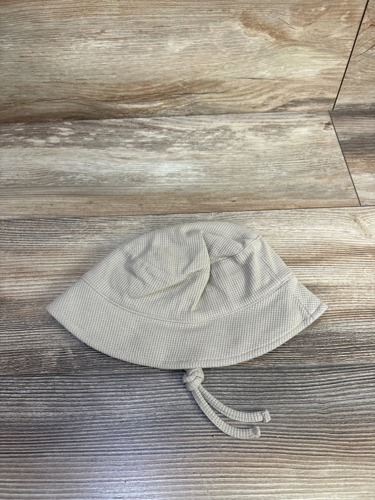Top-down view of baby waffle knit beige bucket hat showing textured knit and knotted chin ties on wood-grain background