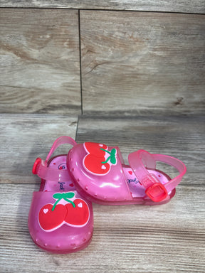 Angled view of Cat & Jack pink toddler jelly sandals showcasing red cherry appliques and adjustable ankle buckle on wooden surface