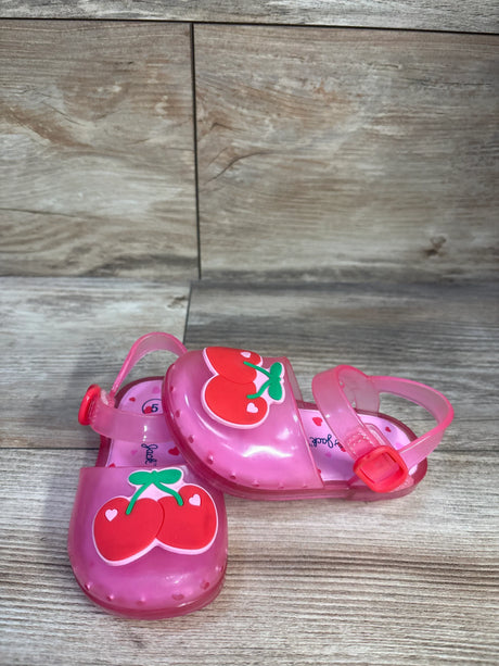Angled view of Cat & Jack pink toddler jelly sandals showcasing red cherry appliques and adjustable ankle buckle on wooden surface