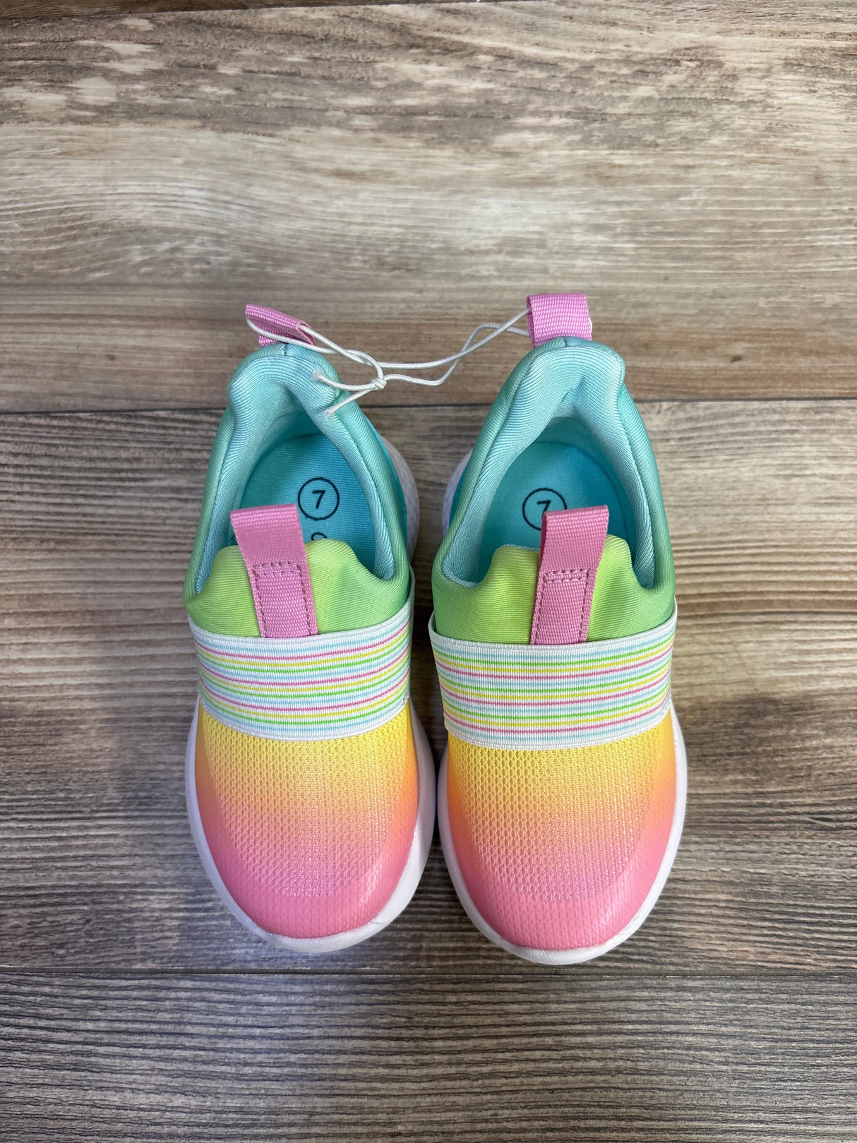 Top view of Cat & Jack rainbow slip-on sneakers with pink-yellow gradient, elastic band, pink tabs, size 7 on wood floor