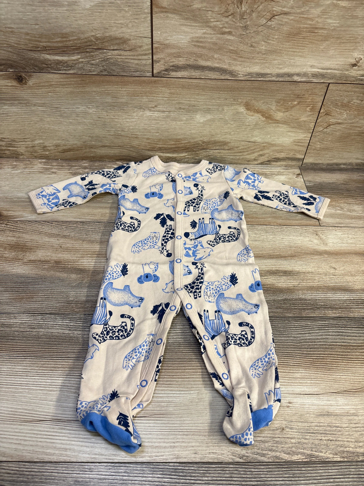 Front view of Carters tan snap sleeper showcasing blue animal print, long sleeves, and covered feet on a wood floor